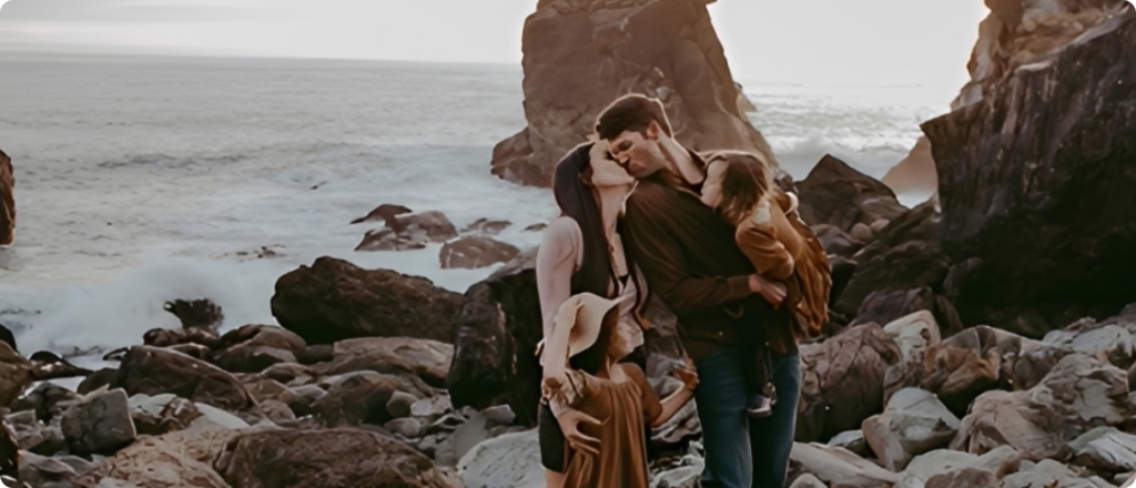 Family embracing on rocky ocean shore.