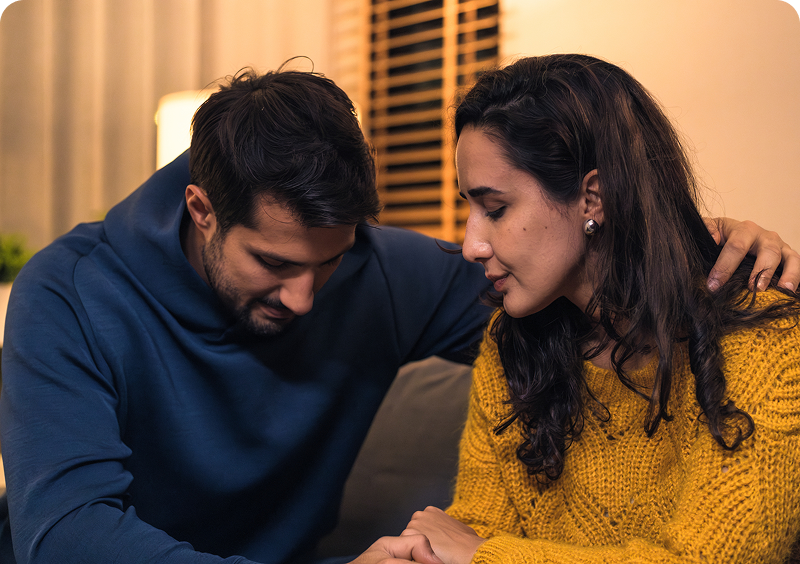 Couple sitting together, looking somber and thoughtful.