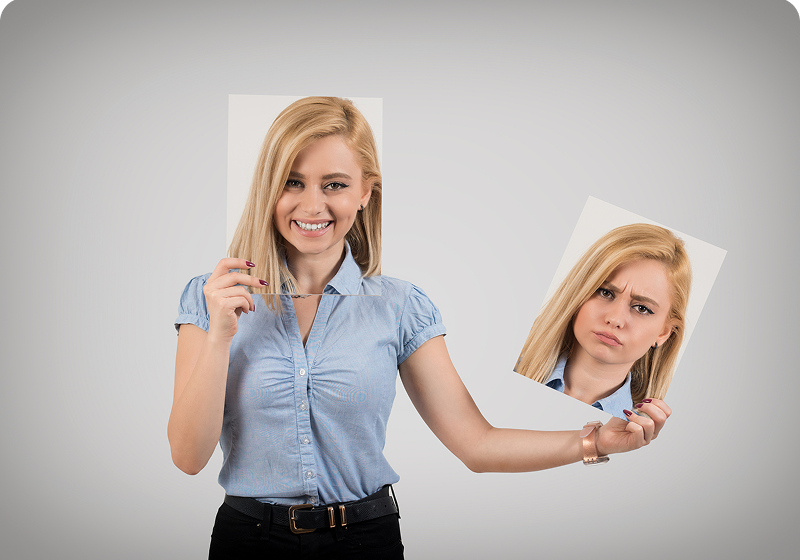 Woman holding two contrasting facial expression photos.