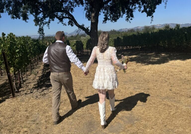 Couple walking in vineyard under tree.