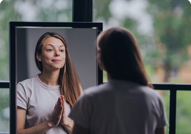 Woman reflecting in mirror, hands clasped together.